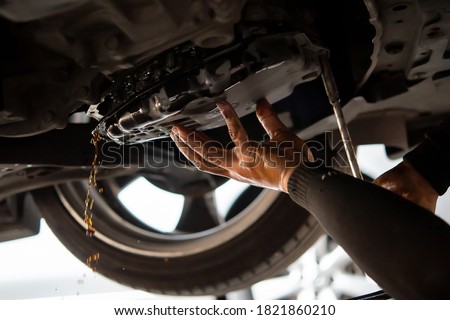 Car mechanic drain the old automatic transmission fluid (ATF) or gear oil at car garage for changing the oil in a gear box of car engine Royalty-Free Stock Photo #1821860210