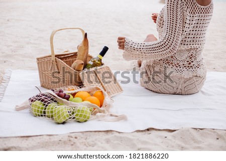 A young woman sits on the beach carpet in a straw hat and a white knitted clothes with back to the camera
  