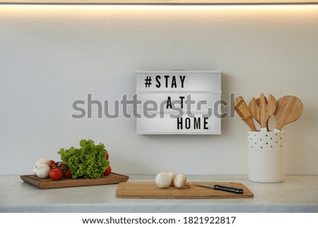 Fresh products, cooking utensils and lightbox with STAY AT HOME in kitchen. Message to promote self-isolation during COVID‑19 pandemic