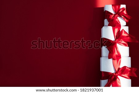 Christmas background. Holiday surprise. Composition of three wrapped white gift boxes with red ribbon bows isolated on burgundy copy space greeting card. New Year congratulation.