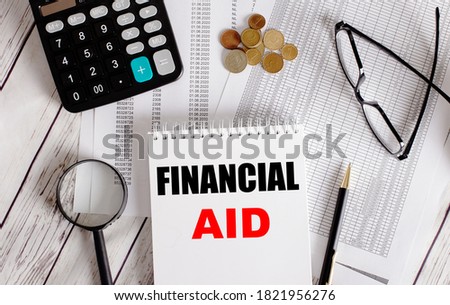 On the table are reports, coins, a calculator, a magnifying glass, a pen, and a notebook with FINANCIAL AID. Financial concept