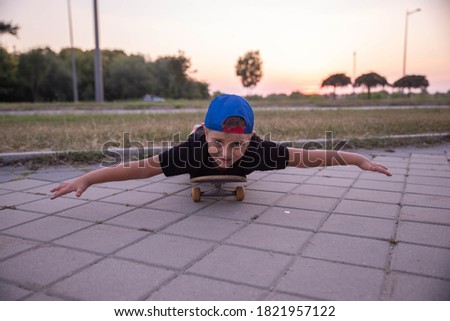 The boy is lying on a skateboard, looking at the camera and spread his arms, simulating an airplane