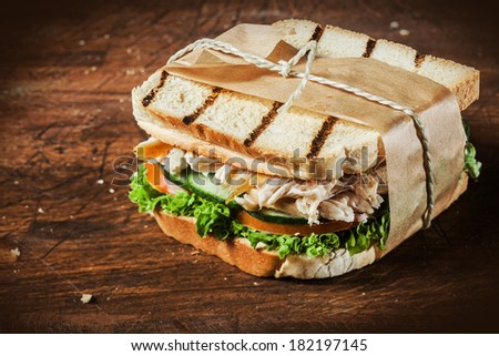 Toasted shredded chicken breast and salad sandwich served on a rustic wooden table wrapped in a brown paper wrapper tied with string with vignetting and copyspace