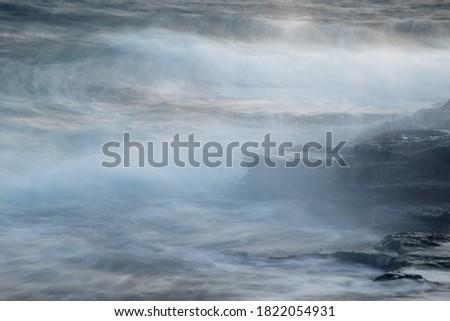 Rocky seashore with wavy ocean and waves crashing on the rocks. Long exposure photography