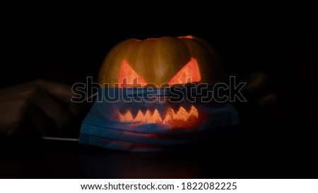 A young woman puts on a protective mask from the virus on a pumpkin at Halloween. Isolated black background.