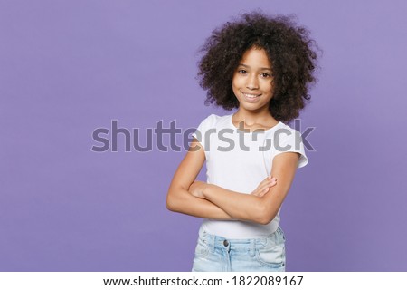 Smiling little african american kid girl 12-13 years old in white t-shirt isolated on pastel violet background studio portrait. Childhood lifestyle concept. Mock up copy space. Holding hands crossed Royalty-Free Stock Photo #1822089167