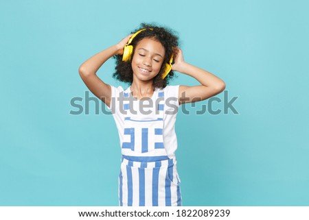 Cute little african american kid girl 12-13 years old in striped clothes isolated on blue background. Childhood lifestyle concept. Mock up copy space. Listen music with headphones keeping eyes closed Royalty-Free Stock Photo #1822089239