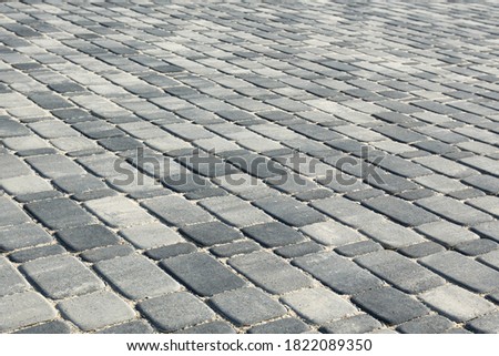 Paving with gray convex road tiles of different sizes (multi-format). The uneven (melange) color of the tile makes it look like natural cobblestone. Perspective point of view.