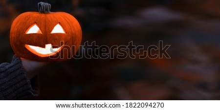 Jack o lantern glowing with moonlight in an eerie night forest.Halloween dark midnight background with burning orange pumpkin that a women holds in his hands.Happy Halloween card.Copyspace for text   