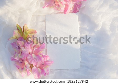 Blank paper card with copy space . Pink gladiolus flower on white textile background. Styled stock photography for display your design, lettering, font, illustration, wedding stationary. Flat lay