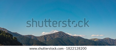 Picture of a mountain on a clear day with white fluffy clouds. There is Mount Fuji on the back with a snowy peak. Feeling calm, cool, relaxing. The idea for cold background with copy space on top.