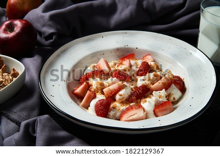 photo of a Breakfast of rice porridge with strawberry slices and nut crumbs on a gray background                               