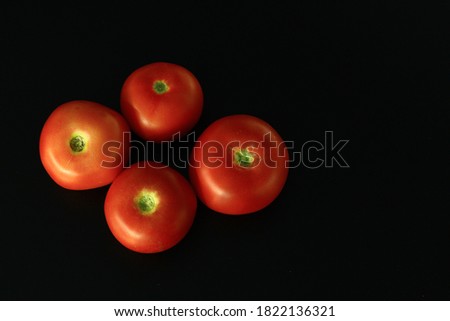 Four red Polish tomatoes on a black background