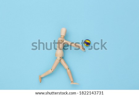 Wooden puppet plays volleyball with ball on blue background