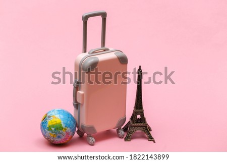 Traveled to Paris. Mini plastic travel suitcase and statuette of the Eiffel Tower, globe on pink background.