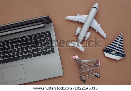 Delivery, online shopping. Laptop and sailboat, shopping trolley, air plane on brown background. Top view. Flat lay
