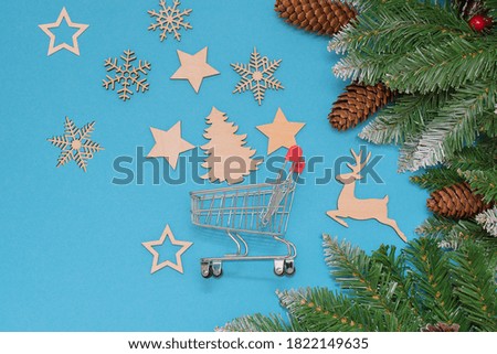 on a blue background fir branches with cones, a mini trolley from the supermarket and wooden Christmas toys in the form of snowflakes, stars, a deer and a Christmas tree. Idea -buying ecological toys.