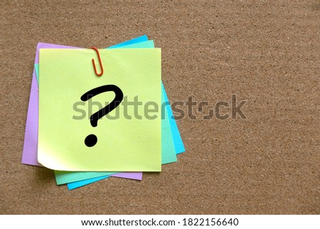 A stack of colorful memo notes written with question symbol ? on a cork board.