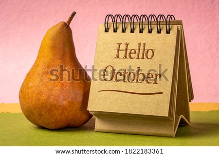 Hello October welcome note  - handwriting in a spiral sketchbook against colorful hndmade paper with a bosc pear, season and calendar concept