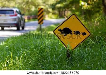 A road sign at a wildlife refuge that warns the drivers of wild animals crossing the road. It aims to prevent animals getting hit by cars. Sign shows a mother turtle and baby turtles crossing the road Royalty-Free Stock Photo #1822186970