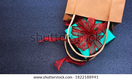 Top angle view green glitter gift box with red ribbon spill out of shopping bag on black table