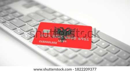 Plastic card depicting flag of Albania on computer keyboard. Fictional numbers