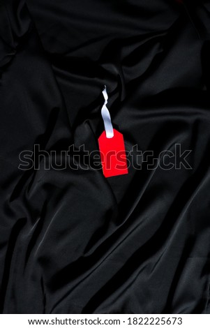Red clothing tag with white ribbon on a black fabric.