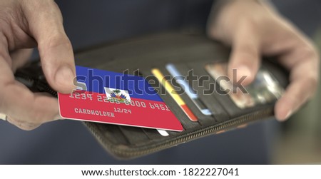 Pulling plastic bank card with flag of Haiti out of the wallet, fictional card number