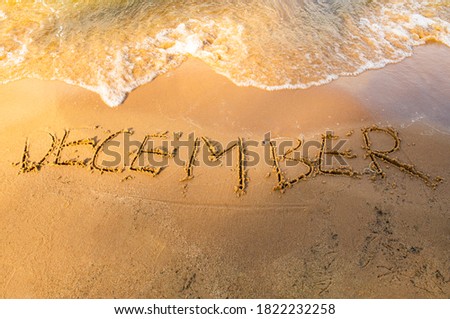 The word DECEMBER written on a yellow sandy shore near the sea