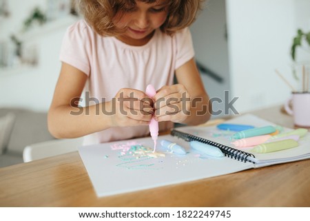 Little girl, preschooler, child painting at the table in a white living room at home close up on paint in tubes selective focus. Home schooling concept