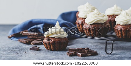 Chocolate cupcakes with cap of cheese cream on metal grid with blue napkin on gray background