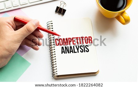 Hand with red pen. Cofee cup. Stick. Keyboard and white background. COMPETITOR ANALYSIS sign in the notepad