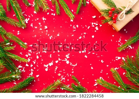 Gift in craft paper with green branches of a Christmas tree and red berries on a red background. Flat lay. Copy space.