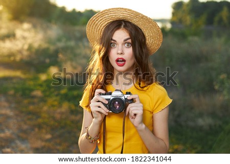 Enamored woman holding a camera in her hands hat red lips yellow t-shirt fresh air