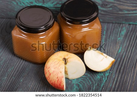 Apple jam in jars. Nearby are apple slices. On brushed black-green boards.
