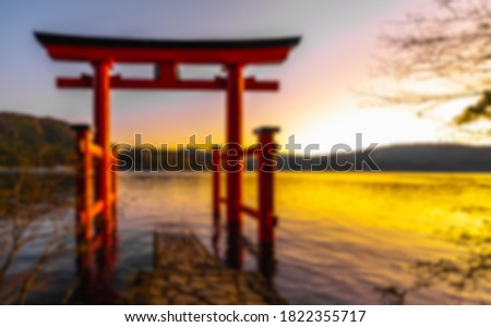 Blur photo of Heiwa no Torii in the lake at Hakone, Japan. The sun is setting, making the sky twilight color in the evening. There are mountains behind and grey cement ladder leaning into the water.