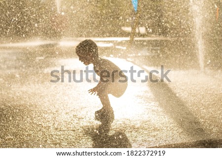 Children at water playground of urban amusement park. Little boy is having fun with water. Little kid having fun playing with water from fountain in evening sunlight. Selective focus. Focus on drops  Royalty-Free Stock Photo #1822372919