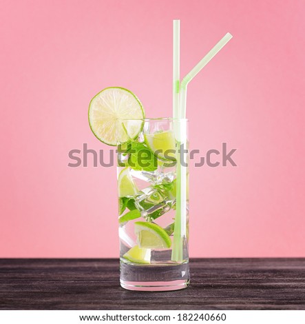 Glass of mojito cocktail on pastel pink background.