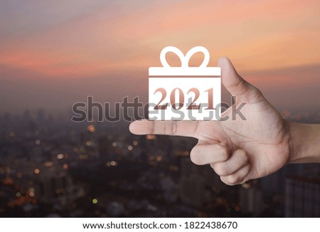 Gift box happy new year 2021 flat icon on finger over blur of cityscape on warm light sundown, Business shopping online concept