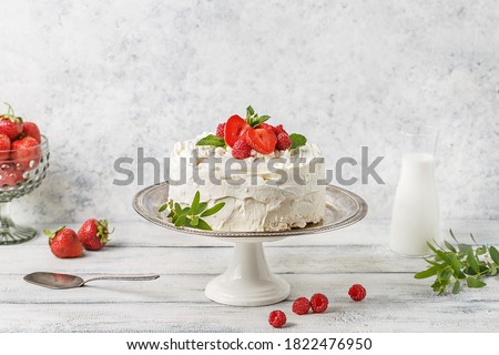 Small cake with white cream decorated with strawberries and raspberries on cake stand over white background with bottle of milk and fresh berries. Side view, copy space Royalty-Free Stock Photo #1822476950
