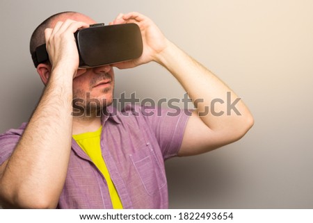 serious man wearing a pair of vr glasses, holding them in his hands with neutral background