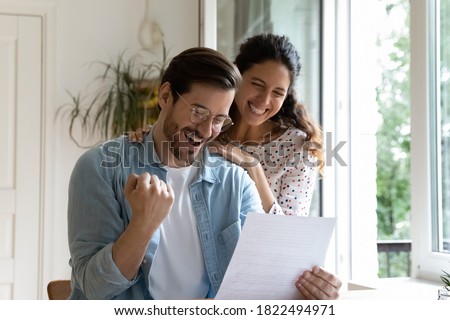 Happy millennial Caucasian couple feel excited euphoric reading amazing pleasant news in paper letter correspondence. Overjoyed man and woman get positive bank response in post paperwork or agreement. Royalty-Free Stock Photo #1822494971