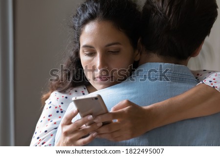 Close up of bored young Caucasian woman hug man texting messaging with lover on smartphone online. Unhappy wife embrace husband cheating on web on cellphone. Family, relationship problem concept.