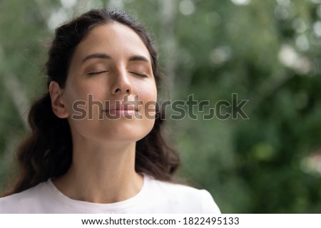 Close up of happy young Caucasian woman isolated on blurred background dream visualize with eyes closed. Smiling dreamy female breathe fresh air relieve negative emotions. Stress free concept. Royalty-Free Stock Photo #1822495133