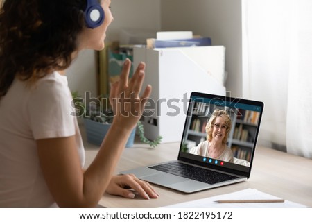 Close up side view of happy woman in headphones look at laptop screen wave greet talk on video call with mature mother. Smiling young female in earphones have pleasant webcam conference on computer. Royalty-Free Stock Photo #1822495172