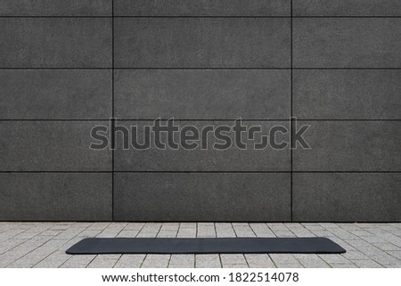empty and blank foldable black yoga mat on grey sidewalk near empty street outdoor in front of grungy concrete textured wall with copy space is a perfect backdrop for text and yoga fitness graphics Royalty-Free Stock Photo #1822514078