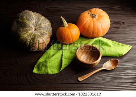 Fresh autumn pumpkins for pumpkin cream soup cooking, wooden bowl and spoon on dark table background