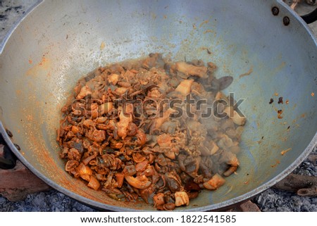 Pork chitterlings meat pieces being cooked in a large frying pan making pork curry for serving to a large number of people.