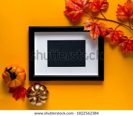 Mock up black frame with maple branches and pumpkin decor on orange background. Autumn concept. Place for text.