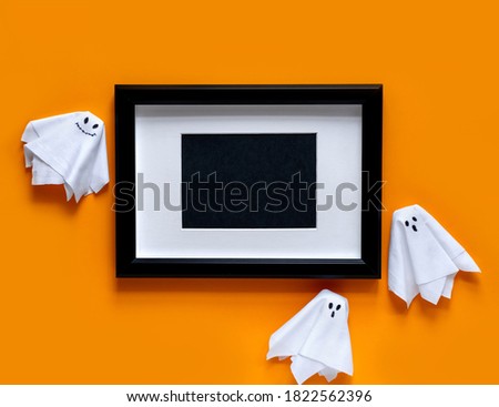 Mock up black frame with ghosts on orange background . Halloween party greeting card mockup with copy space. Flat lay, top view.